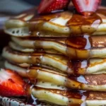 Stack of golden pancakes drizzled with syrup and topped with fresh berries