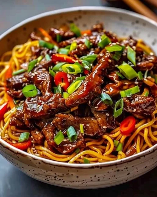 Delicious bowl of sticky beef noodles garnished with fresh herbs
